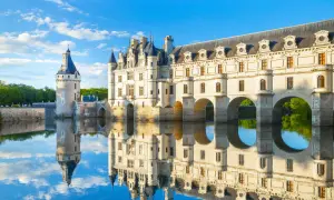 Le château de Chenonceau, joyau des monuments de la Loire, se reflète dans l'eau paisible sous un ciel bleu.