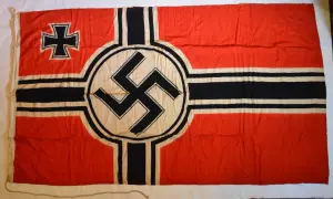 Drapeau rouge avec une croix noire et blanche dans le coin supérieur gauche et une croix gammée noire sur un cercle blanc au centre. L'origine de la croix gammée est complexe.