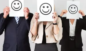 Trois personnes en tenue professionnelle cachent leur visage derrière des feuilles avec des smiley. Le bonheur est une idée neuve en Europe, et ces visages souriants le prouvent.