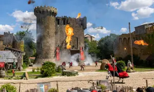 Spectacle de feu et de chevaliers devant le **château du Puy du Fou**. Des flammes jaillissent du donjon, des combattants s'affrontent.