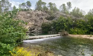 La source du Lez, une cascade artificielle sur une rivière bordée de falaises rocheuses et de végétation luxuriante.