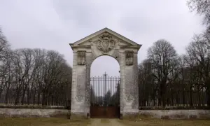 Portail monumental menant au **château de Richelieu**, avec une grille en fer forgé et des arbres dénudés en arrière-plan.