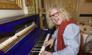 Jean-Pierre Chalencon, avec sa chevelure blonde et ses lunettes, joue du piano bleu électrique, l'air joyeux.
