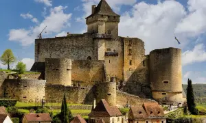 Un château médiéval impressionnant, l'un des célèbres châteaux en France, se dresse sur une colline verdoyante, sous un ciel bleu parsemé de nuages.