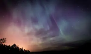 Ciel étoilé aux couleurs de l'aurore boréale, une harmonie du soir qui évoque Baudelaire. Silhouettes d'arbres et de collines dans la nuit.