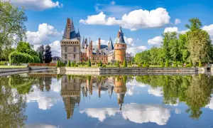 Magnifique château en Eure-et-Loir, reflet parfait dans l'eau calme, entouré de jardins à la française et d'arbres verdoyants sous un ciel bleu parsemé de nuages.
