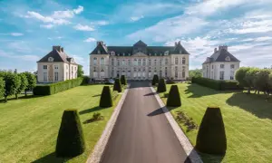 Le majestueux château de Brienne, avec ses ailes symétriques et son allée bordée de topiaires, sous un ciel bleu éclatant.