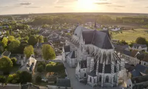 Vue aérienne de la basilique de Cléry-Saint-André au coucher du soleil, baignant le village et ses toits dans une lumière dorée.