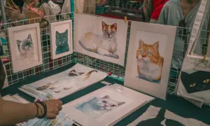 Des tableaux de chats, des portraits de félins aux regards expressifs, comme les chats Baudelaire, sont exposés sur un étal.