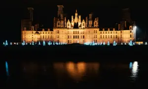 Un château illuminé la nuit, bordé de sapins bleus scintillants, évoque la magie de Noël aux Châteaux de la Loire.