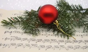 Boule rouge sur partition de "Minuit Chrétien", entourée de branches de sapin givrées. La musique de Noël prend vie.