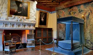 Intérieur du château de Chenonceau : cheminée monumentale, portraits, lit à baldaquin bleu et tapisseries somptueuses.