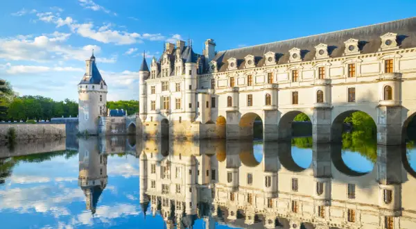 Le château de Chenonceau, joyau des monuments de la Loire, se reflète dans l'eau paisible sous un ciel bleu.