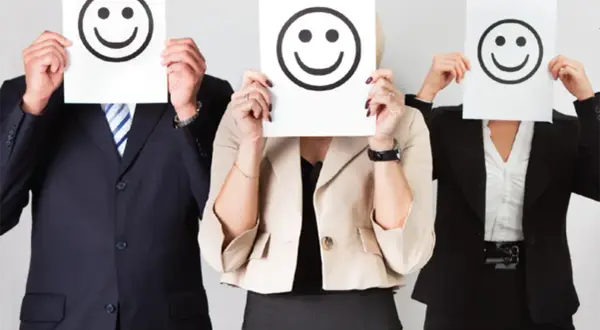 Trois personnes en tenue professionnelle cachent leur visage derrière des feuilles avec des smiley. Le bonheur est une idée neuve en Europe, et ces visages souriants le prouvent.