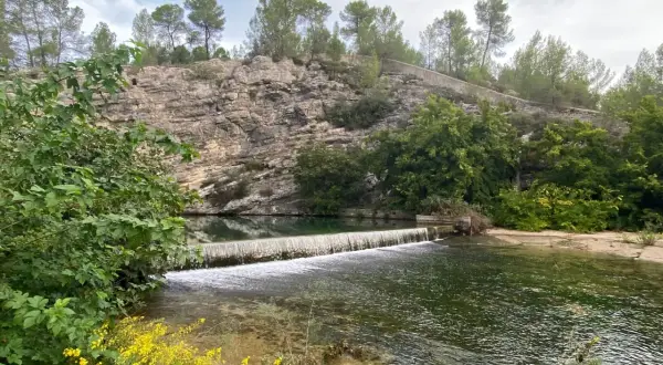 La source du Lez, une cascade artificielle sur une rivière bordée de falaises rocheuses et de végétation luxuriante.