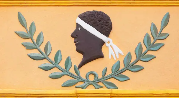 Bas-relief d'une tête d'homme noir, ornée d'un bandeau blanc, entourée de feuilles de laurier. Une évocation des maures origine.
