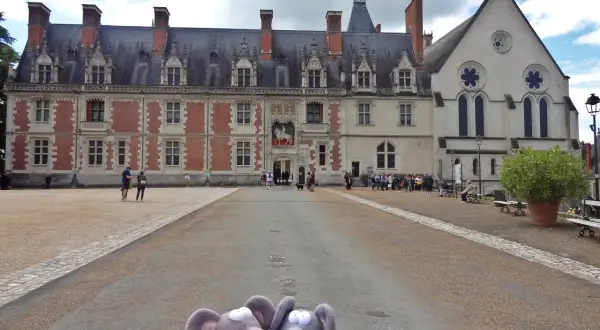 Deux souris en peluche posent devant la majestueuse place du château de Blois, avec son architecture Renaissance et gothique.