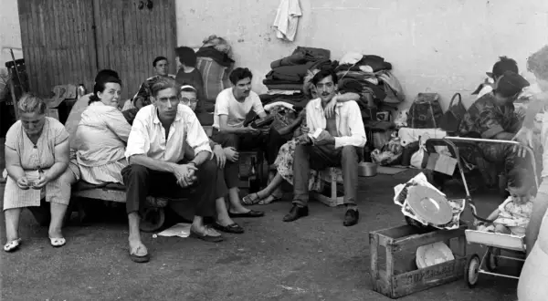 Un groupe de personnes, dont des hommes, des femmes et un bébé, attendent, reflétant le caractère des pieds-noirs dans l'attente.