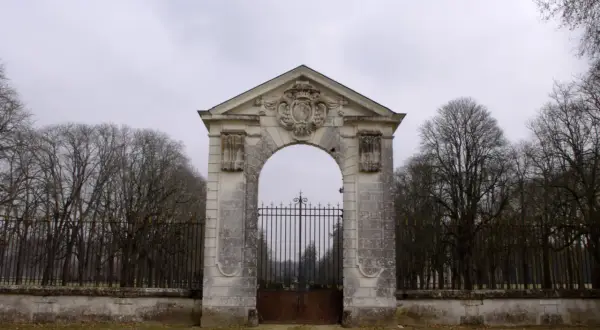 Portail monumental menant au **château de Richelieu**, avec une grille en fer forgé et des arbres dénudés en arrière-plan.