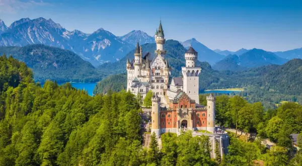 Le château de Neuschwanstein, un joyau parmi le top 10 des plus grands châteaux du monde, se dresse majestueusement sur une colline boisée, dominant un lac bleu et des montagnes imposantes.