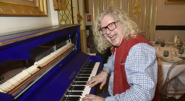 Jean-Pierre Chalencon, avec sa chevelure blonde et ses lunettes, joue du piano bleu électrique, l'air joyeux.