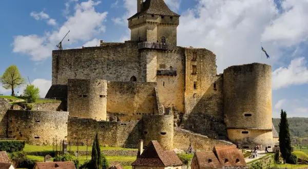 Un château médiéval impressionnant, l'un des célèbres châteaux en France, se dresse sur une colline verdoyante, sous un ciel bleu parsemé de nuages.