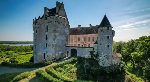 Le majestueux **château du Bouchet** se dresse fièrement sur une colline verdoyante, dominant un lac paisible sous un ciel bleu éclatant.