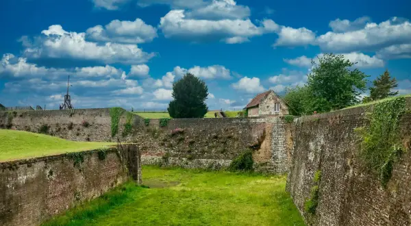 Murs de pierre et de brique du château de Montreuil, envahis par la végétation, sous un ciel bleu et nuageux.