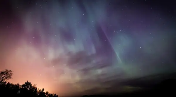 Ciel étoilé aux couleurs de l'aurore boréale, une harmonie du soir qui évoque Baudelaire. Silhouettes d'arbres et de collines dans la nuit.