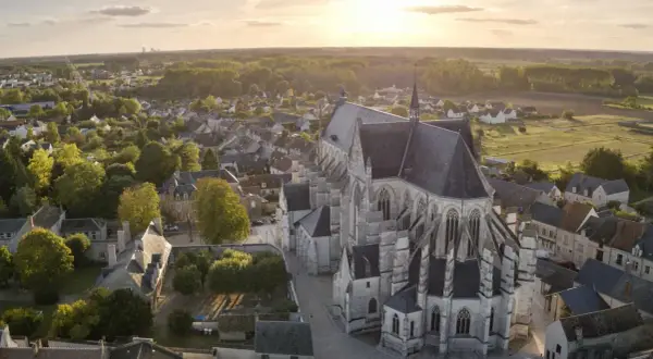 Vue aérienne de la basilique de Cléry-Saint-André au coucher du soleil, baignant le village et ses toits dans une lumière dorée.