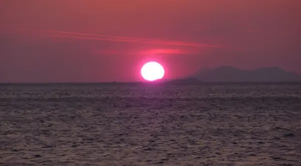 Un soleil couchant victor hugo, d'un rose intense, se reflète sur la mer calme, baignant le paysage d'une lumière poétique.