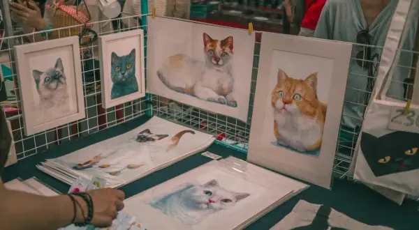 Des tableaux de chats, des portraits de félins aux regards expressifs, comme les chats Baudelaire, sont exposés sur un étal.