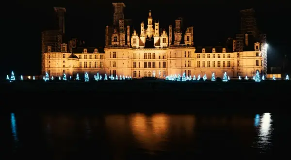 Un château illuminé la nuit, bordé de sapins bleus scintillants, évoque la magie de Noël aux Châteaux de la Loire.