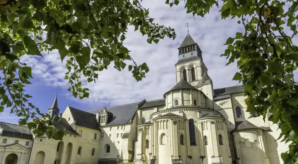 L'abbaye de Fontevraud, vue à travers des feuilles vertes. Combien de temps pour visiter Fontevraud ? Prévoyez une journée entière pour explorer ce site historique.