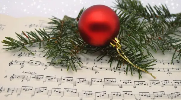 Boule rouge sur partition de "Minuit Chrétien", entourée de branches de sapin givrées. La musique de Noël prend vie.