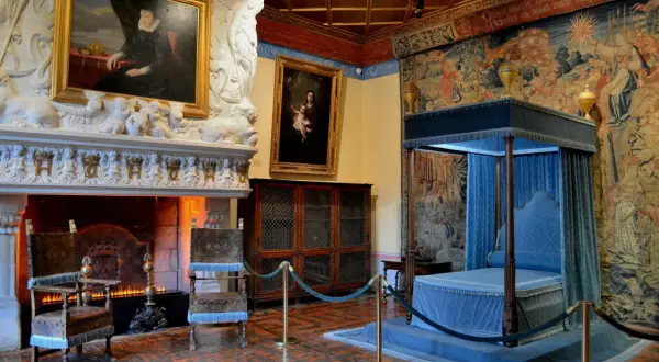 Intérieur du château de Chenonceau : cheminée monumentale, portraits, lit à baldaquin bleu et tapisseries somptueuses.