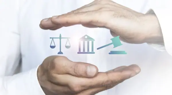 Mains protégeant des icônes symbolisant la justice : balance, bâtiment de tribunal, marteau de juge. L'image évoque l'importance de l'état de droit.