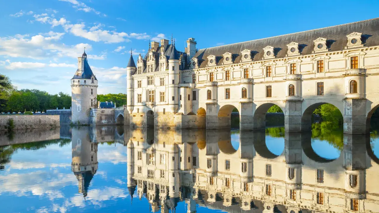 Le château de Chenonceau, joyau des monuments de la Loire, se reflète dans l'eau paisible sous un ciel bleu.