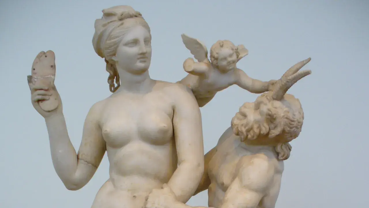 Sculpture grecque antique : Vénus, un putto ailé et un satyre. La déesse tient un objet brisé.