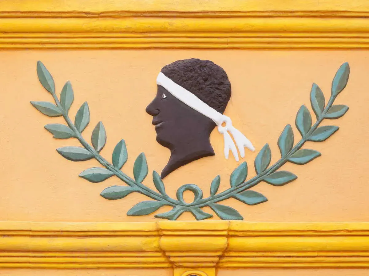 Bas-relief d'une tête d'homme noir, ornée d'un bandeau blanc, entourée de feuilles de laurier. Une évocation des maures origine.