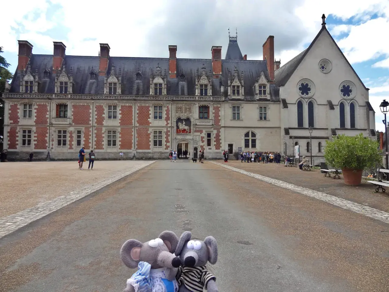 Deux souris en peluche posent devant la majestueuse place du château de Blois, avec son architecture Renaissance et gothique.