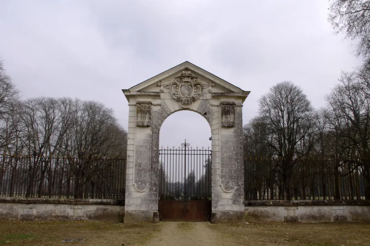 Portail monumental menant au **château de Richelieu**, avec une grille en fer forgé et des arbres dénudés en arrière-plan.