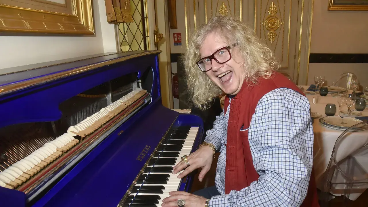 Jean-Pierre Chalencon, avec sa chevelure blonde et ses lunettes, joue du piano bleu électrique, l'air joyeux.