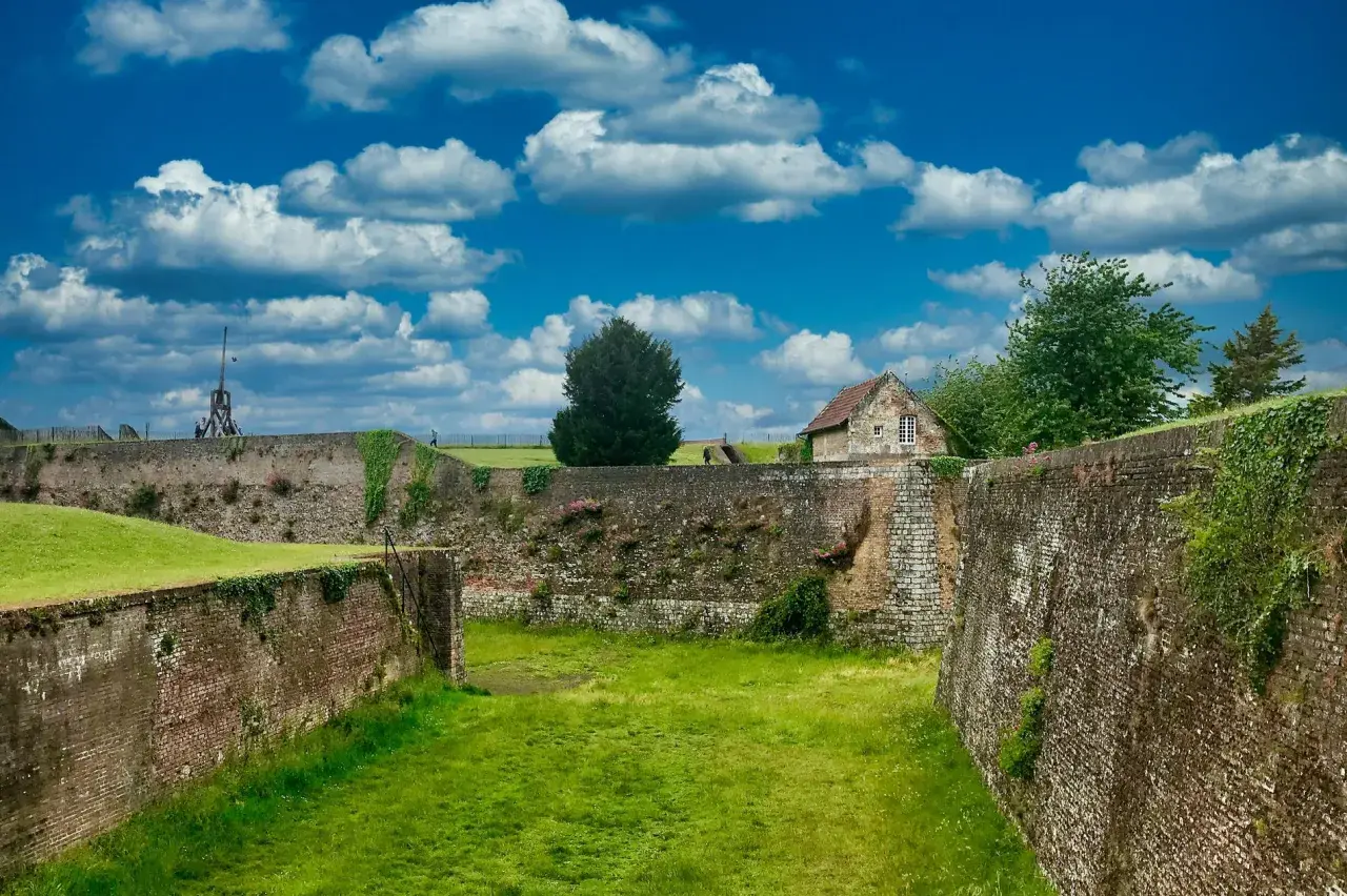 Murs de pierre et de brique du château de Montreuil, envahis par la végétation, sous un ciel bleu et nuageux.