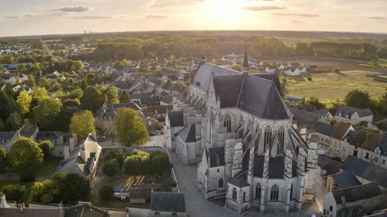 Vue aérienne de la basilique de Cléry-Saint-André au coucher du soleil, baignant le village et ses toits dans une lumière dorée.