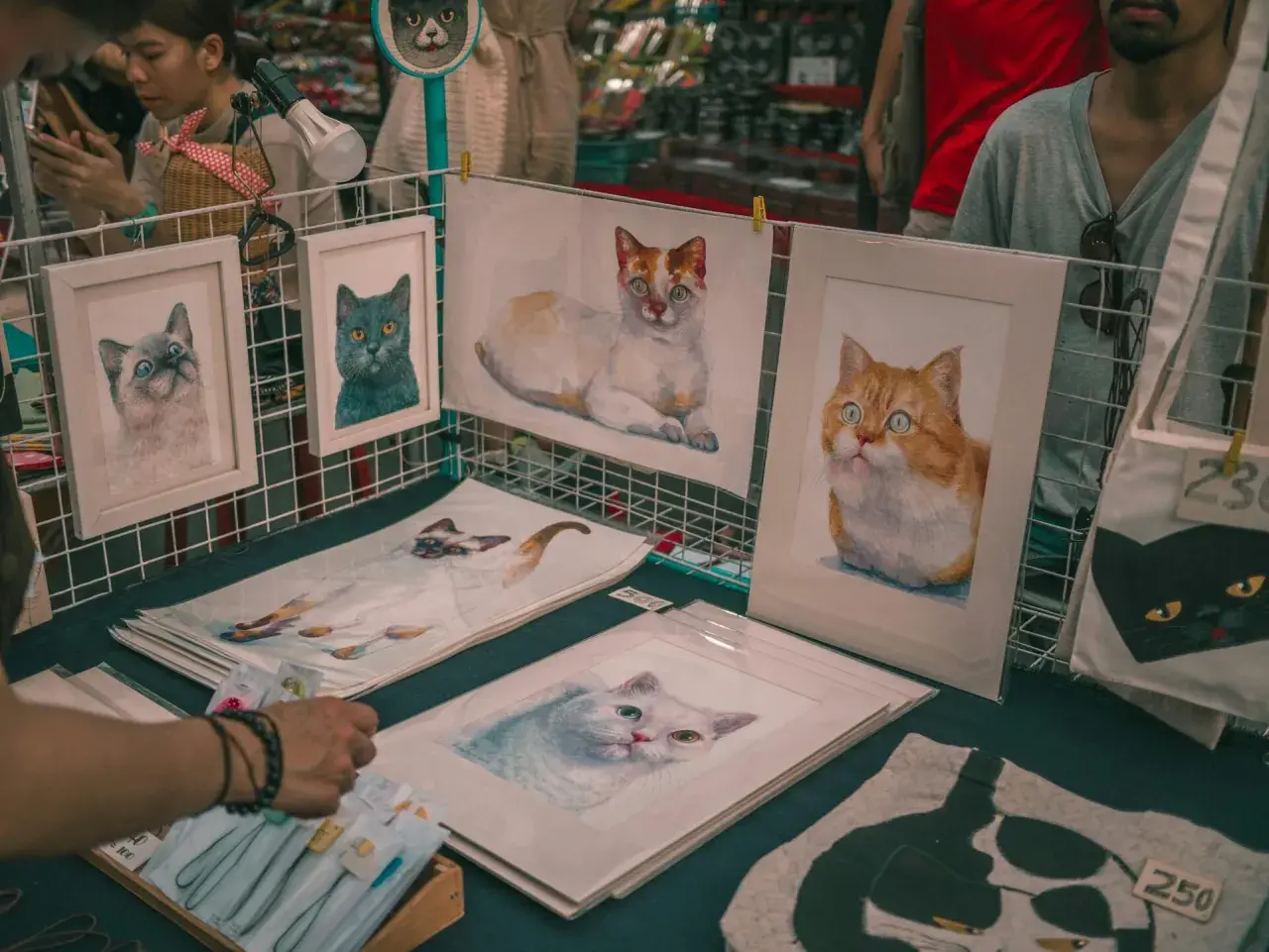 Des tableaux de chats, des portraits de félins aux regards expressifs, comme les chats Baudelaire, sont exposés sur un étal.