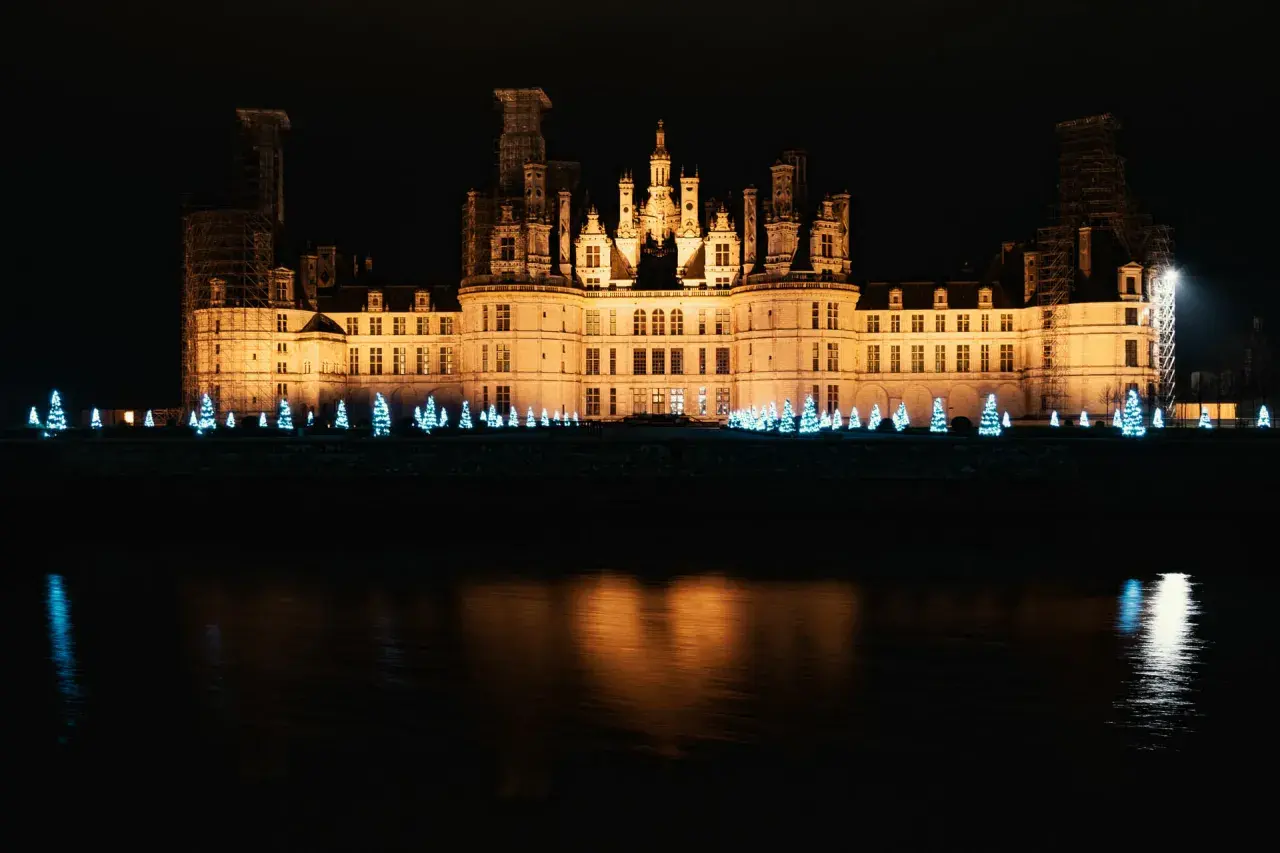 Un château illuminé la nuit, bordé de sapins bleus scintillants, évoque la magie de Noël aux Châteaux de la Loire.