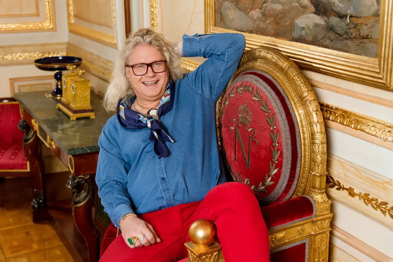 Jean Pierre Chalencon, un homme au style audacieux, pose dans un fauteuil rouge orn&eacute; d'un N imp&eacute;rial.