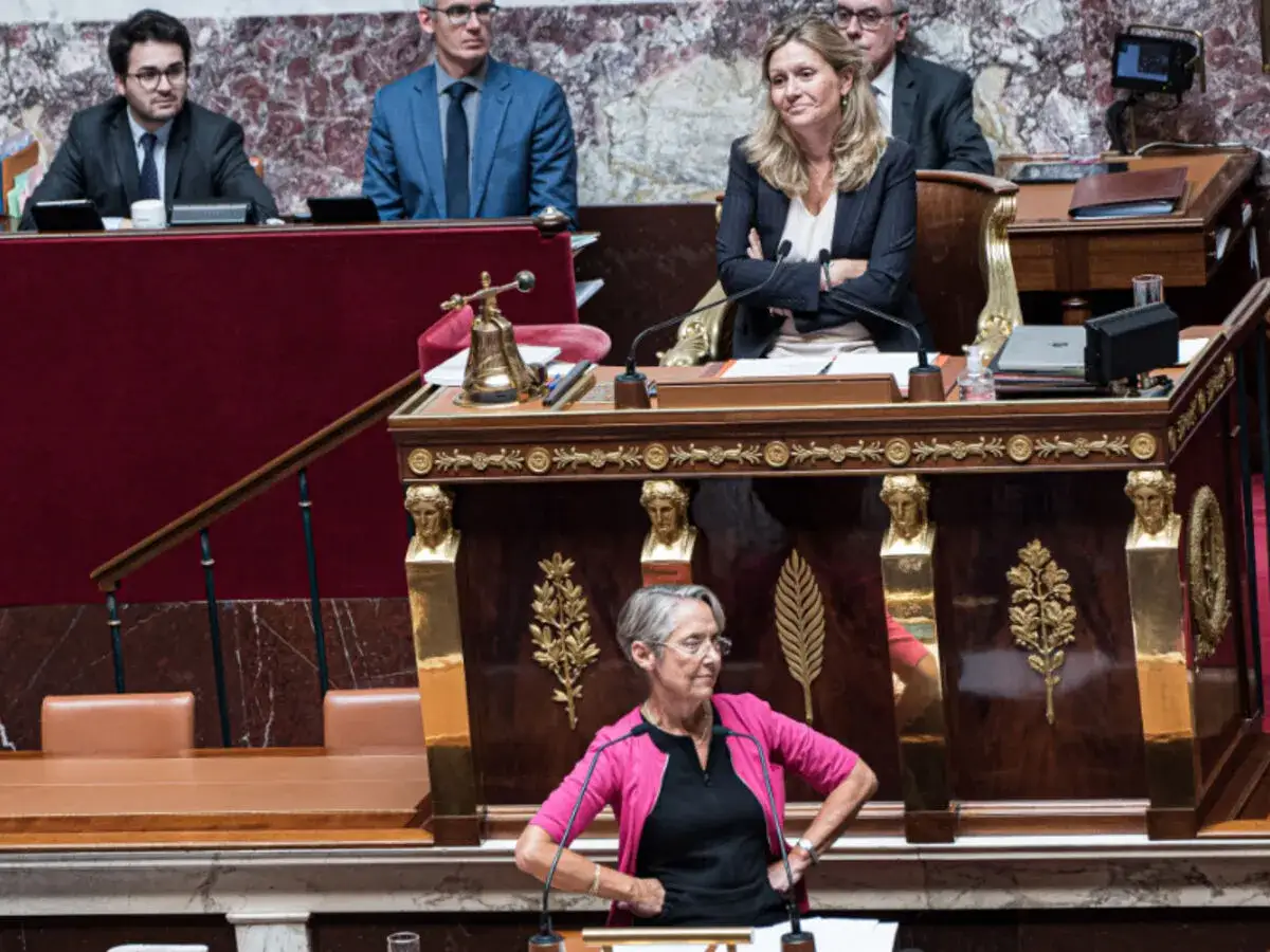Débat intense à l'Assemblée nationale. Une femme en rose s'exprime, tandis que d'autres l'écoutent. Le peuple contre la démocratie, un sujet qui divise.