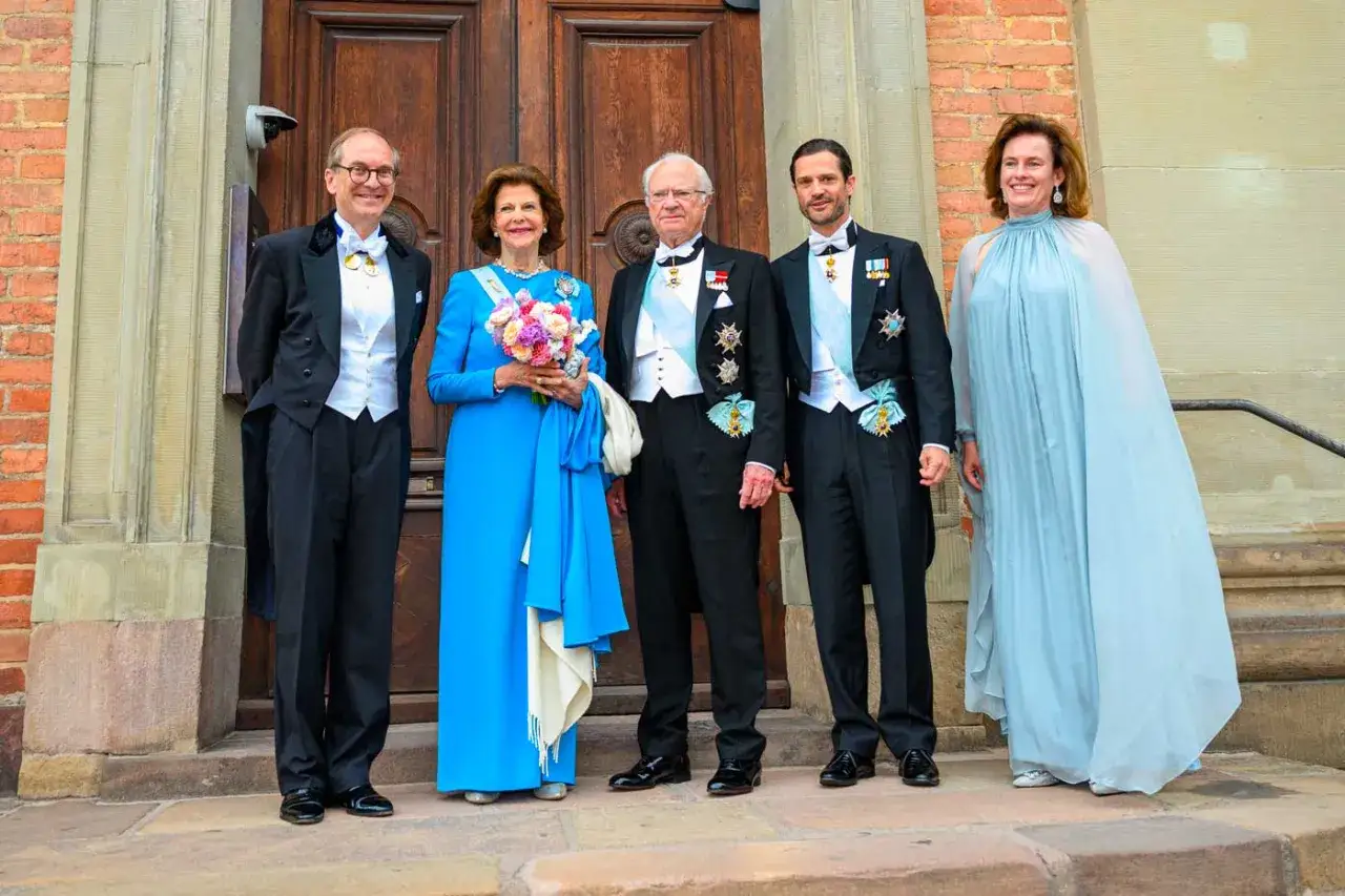 La famille de Sparre, &eacute;l&eacute;gamment v&ecirc;tue, pose devant une porte en bois. La reine Silvia porte une robe bleue et tient un bouquet.